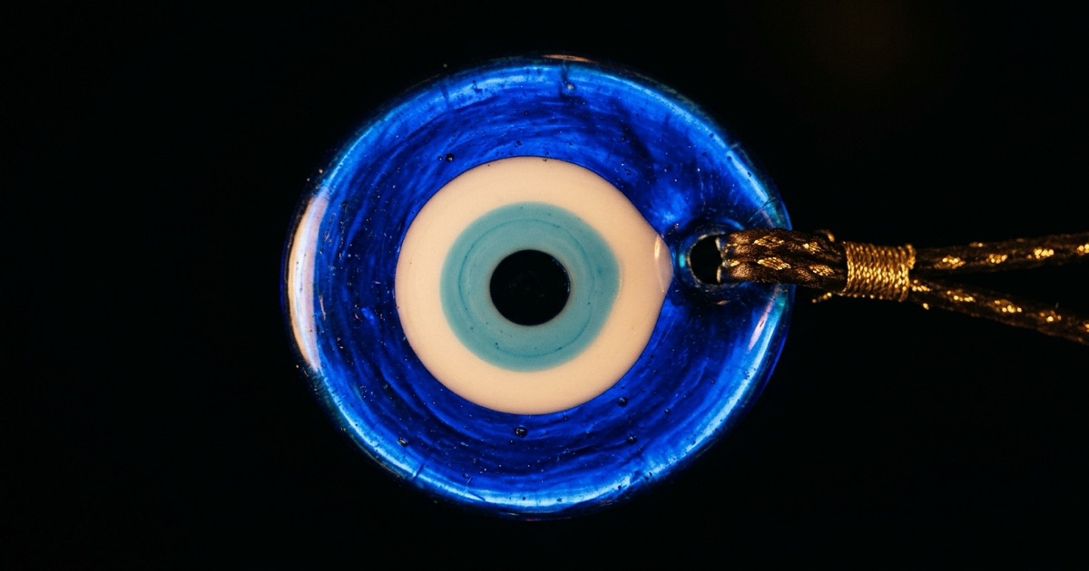 A macro close-up of a single cobalt-blue nazar bead, its concentric rings of white, light blue, and black filling the frame, lit so the glass glows from within against pure black